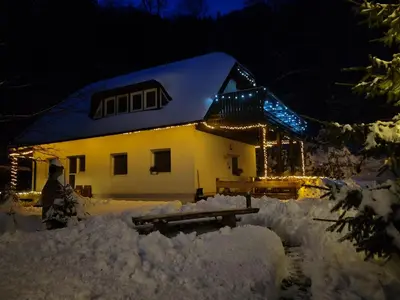 a house covered in snow at night with lights at apartma Pohorc - Praprot in Pohorje