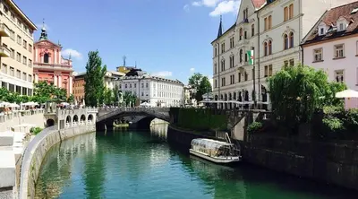 a boat on a river in a city with buildings at Apartman min & Ljubljana in Ljubljana
