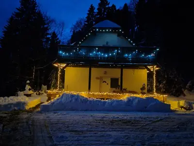 a building with lights in the snow at night at apartma Pohorc - Kostanj in Pohorje