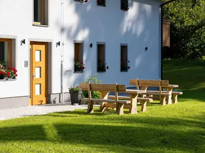two benches sitting in the grass in front of a building at The Woodland Nook Apartments Bohinj - Classic Two Bedroom Apartment with Balcony in Bohinj