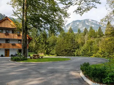 a winding road in front of a building with mountains in the background at The Woodland Nook Apartments Bohinj - Two Bedroom Apartment with Balcony in Bohinj