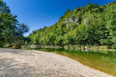 a river with a rocky shore next to a mountain at Riverside Suite Mobile Homes in Gradac