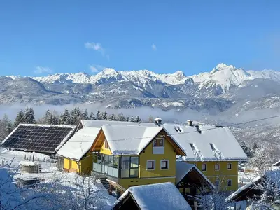 a house with snow on the roof with mountains in the background at SPA Tubej - Adults Only in Bohinj